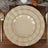 Elegant beige dinnerware set with gold trim, stacked on a wooden table.