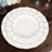 Elegant white dinner plates with gold trim, stacked on a wooden table.