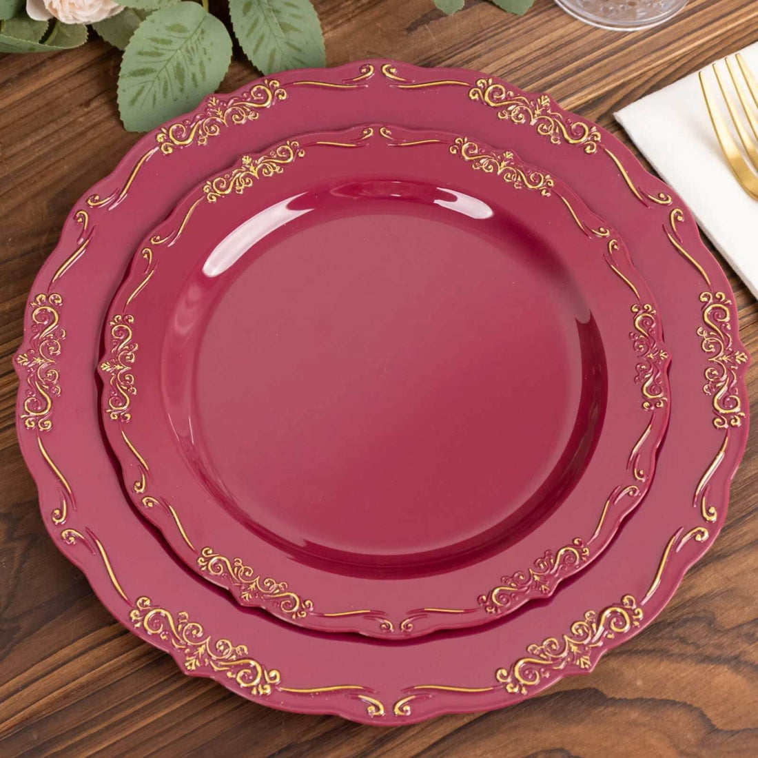 Elegant burgundy dinner plates with gold accents stacked on a wooden table.