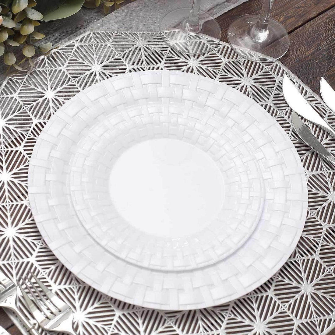White decorative plates on a silver placemat with cutlery.