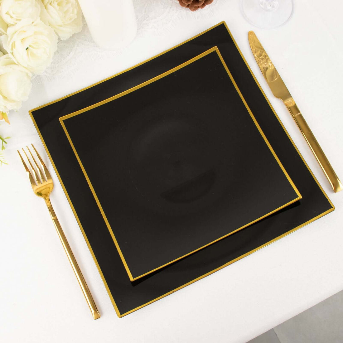 Black dinner plates with gold trim on a white table setting.