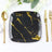 Black square plate with gold marble design, surrounded by elegant cutlery.