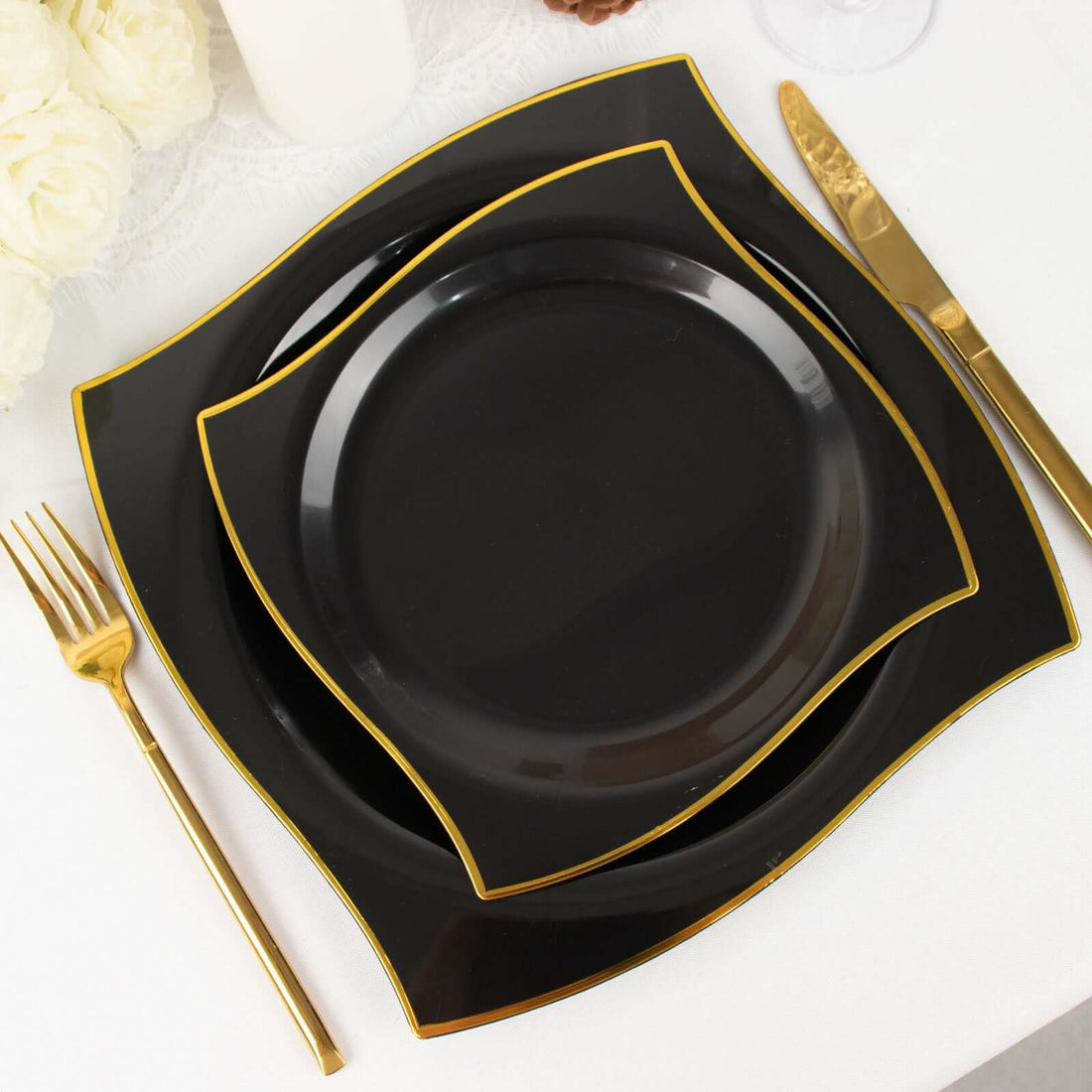 Elegant black plates with gold trim stacked on a white tablecloth.