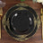 Elegant black plate with gold ornate design on a wooden table setting.