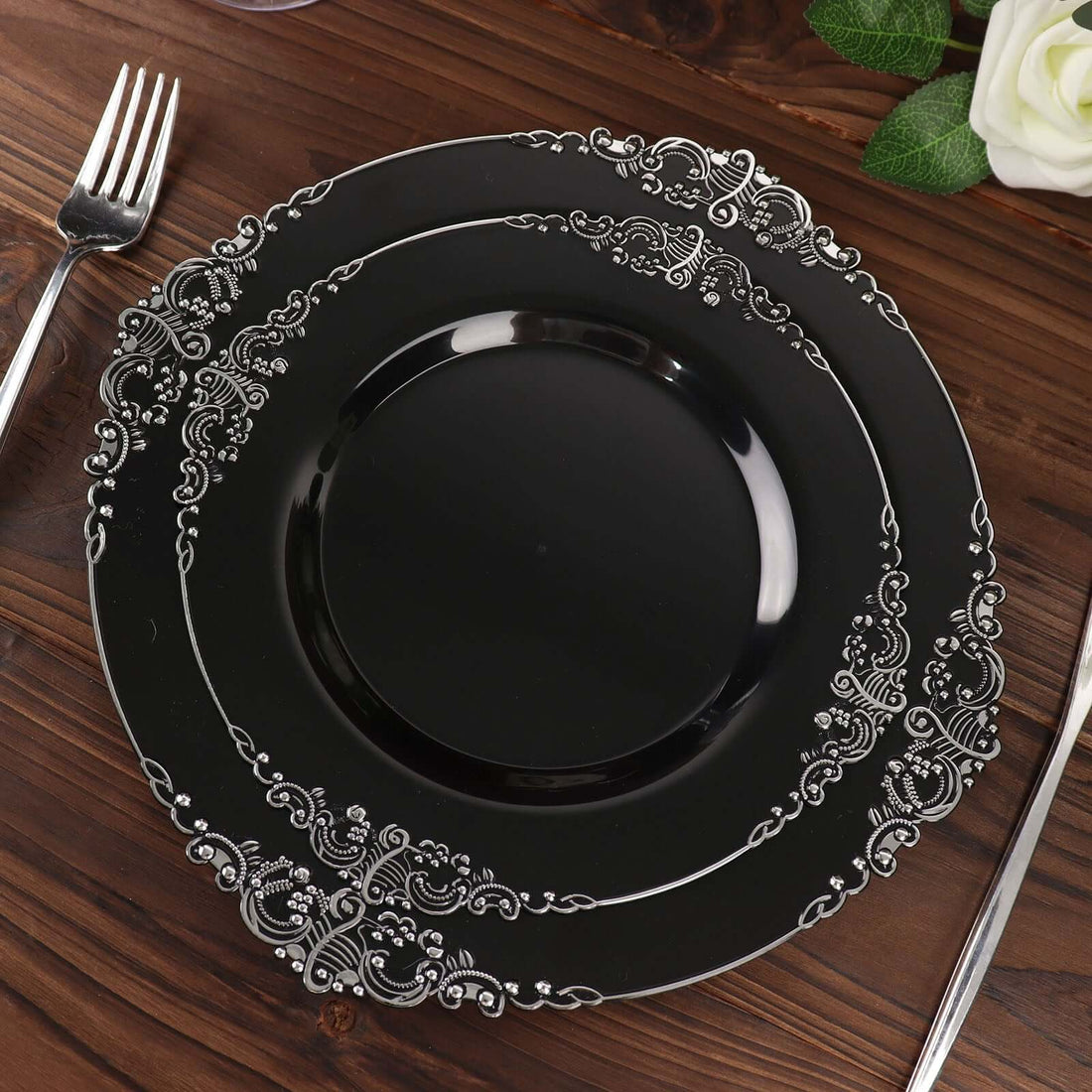 Elegant black plate with ornate silver detailing on a wooden table.