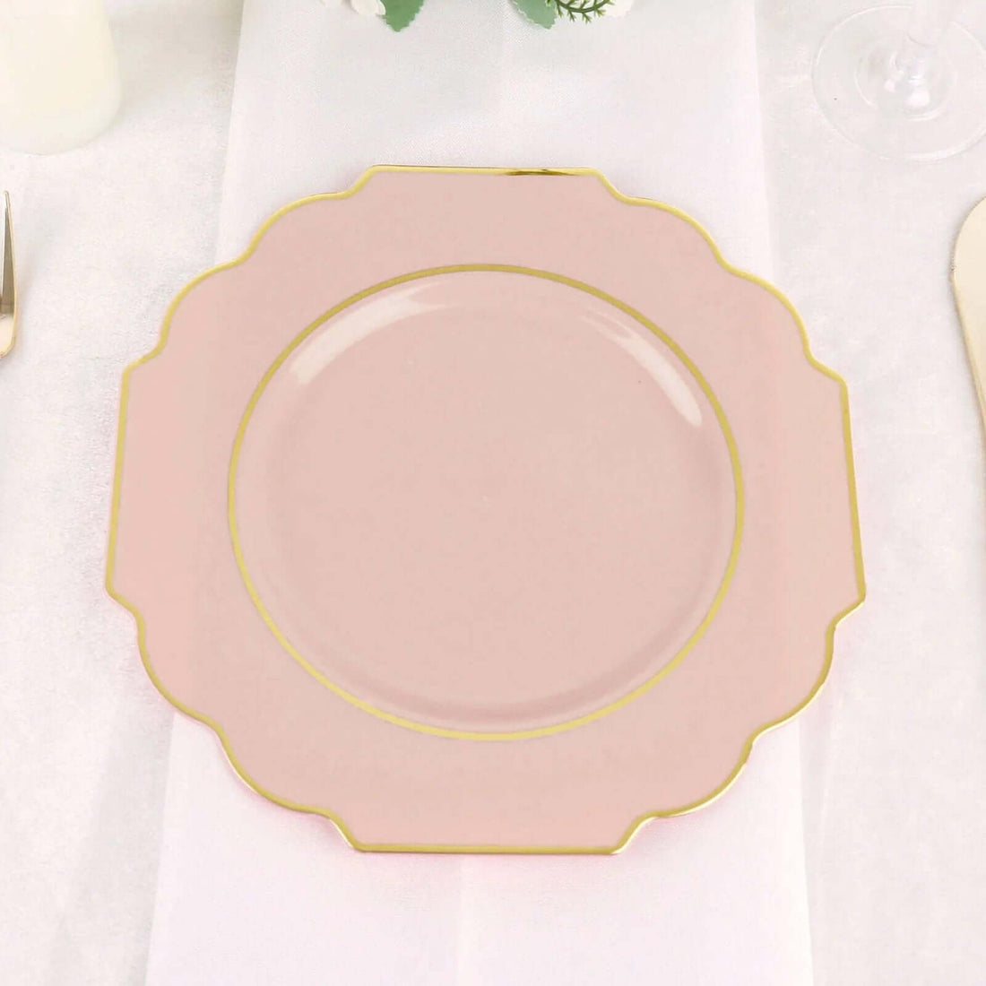 Pink scalloped plate with gold trim on a table setting.