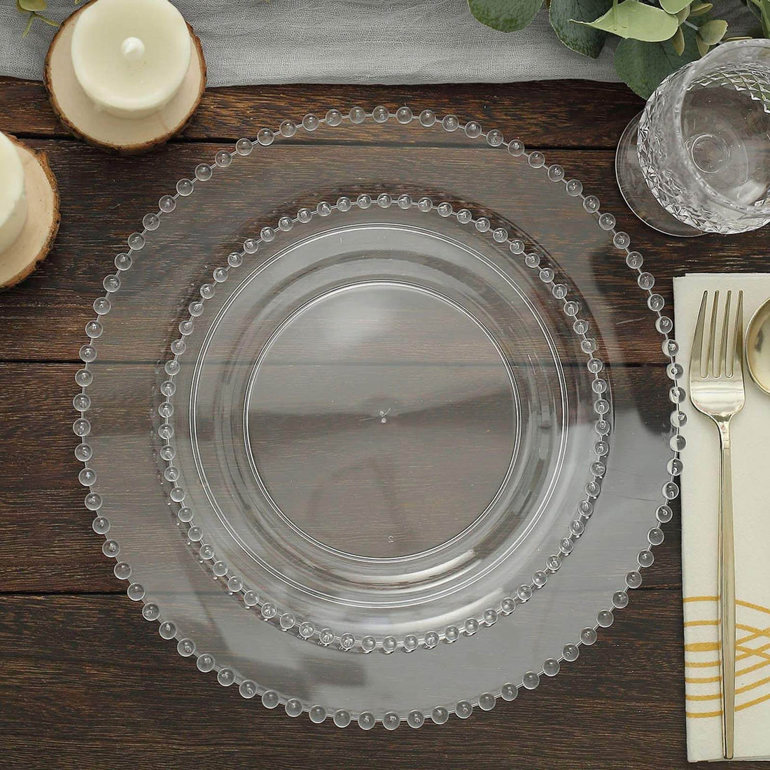 Clear charger plate with beaded rim on a wooden table setting.
