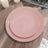 Pink dinner plates with gold trim on a wooden table setting.