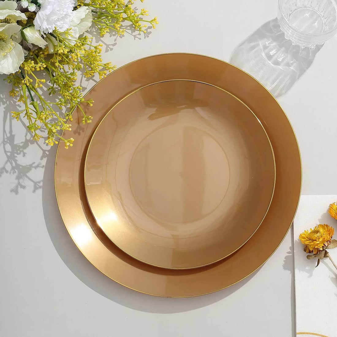 Elegant gold rimmed plates stacked on a table with floral accents.