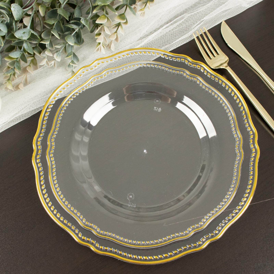 Elegant clear plate with gold trim on a dark wooden table setting.