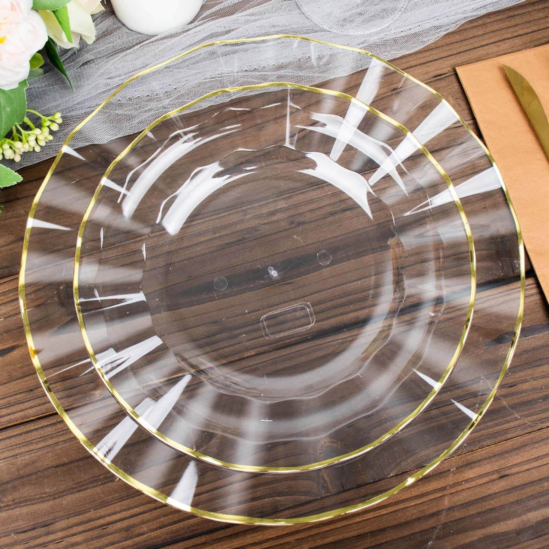 Clear plastic charger plate with gold trim on a wooden table.