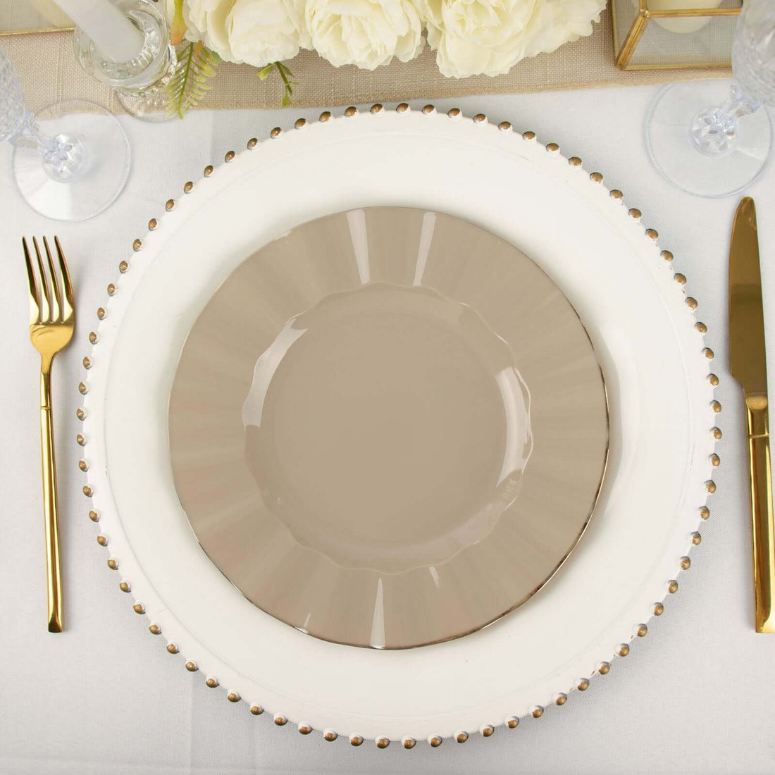 Elegant beige dinner plate on decorative charger with gold utensils.