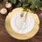 Elegant gold charger plate with white ruffled plate and gold utensils on a wooden table.