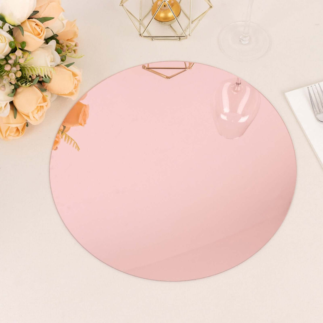 Round rose gold mirror charger plate on a table with flowers and decor.