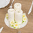 Three white candles surrounded by rose accents on a mirrored base.