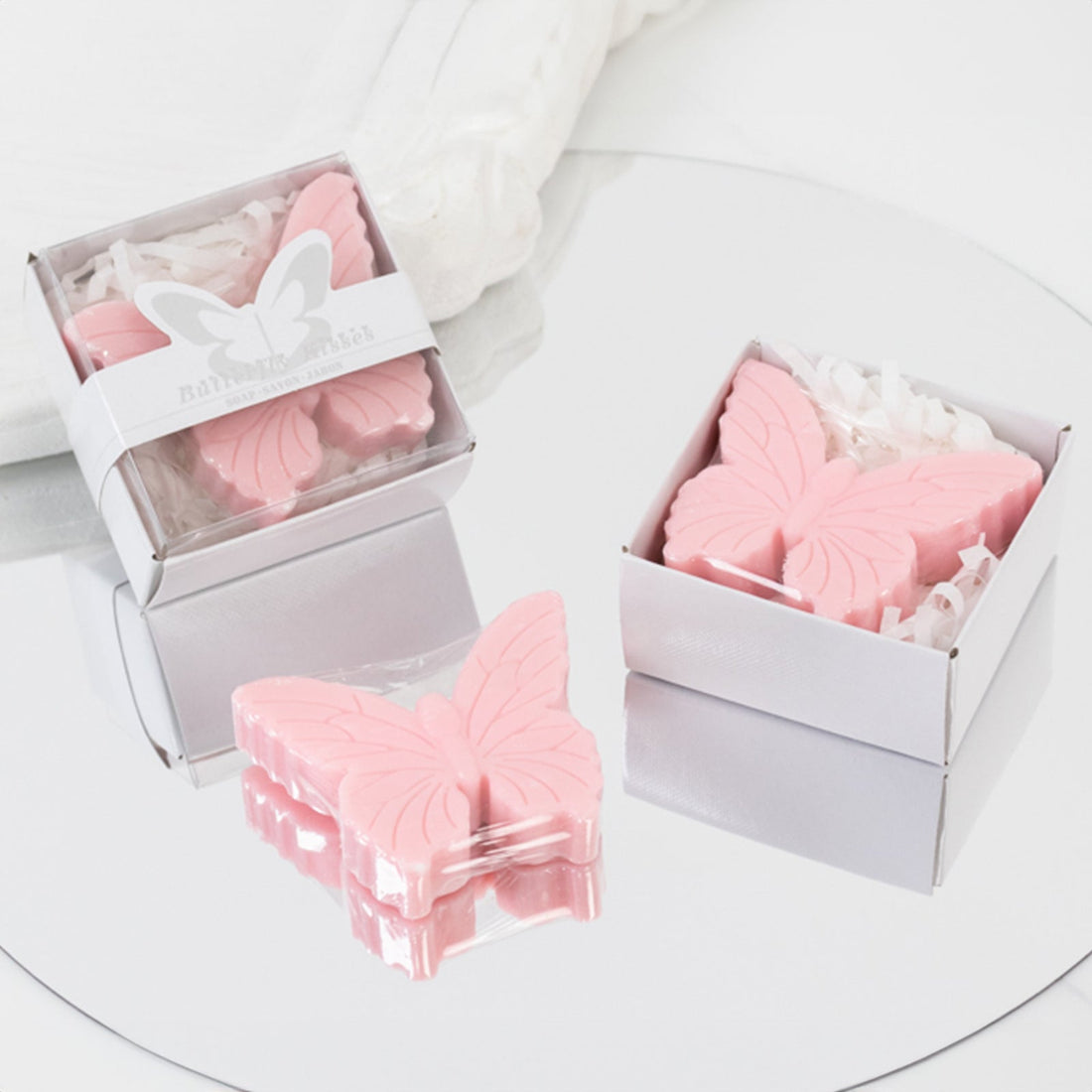 Pink butterfly-shaped wax melts in decorative boxes on a mirrored surface.