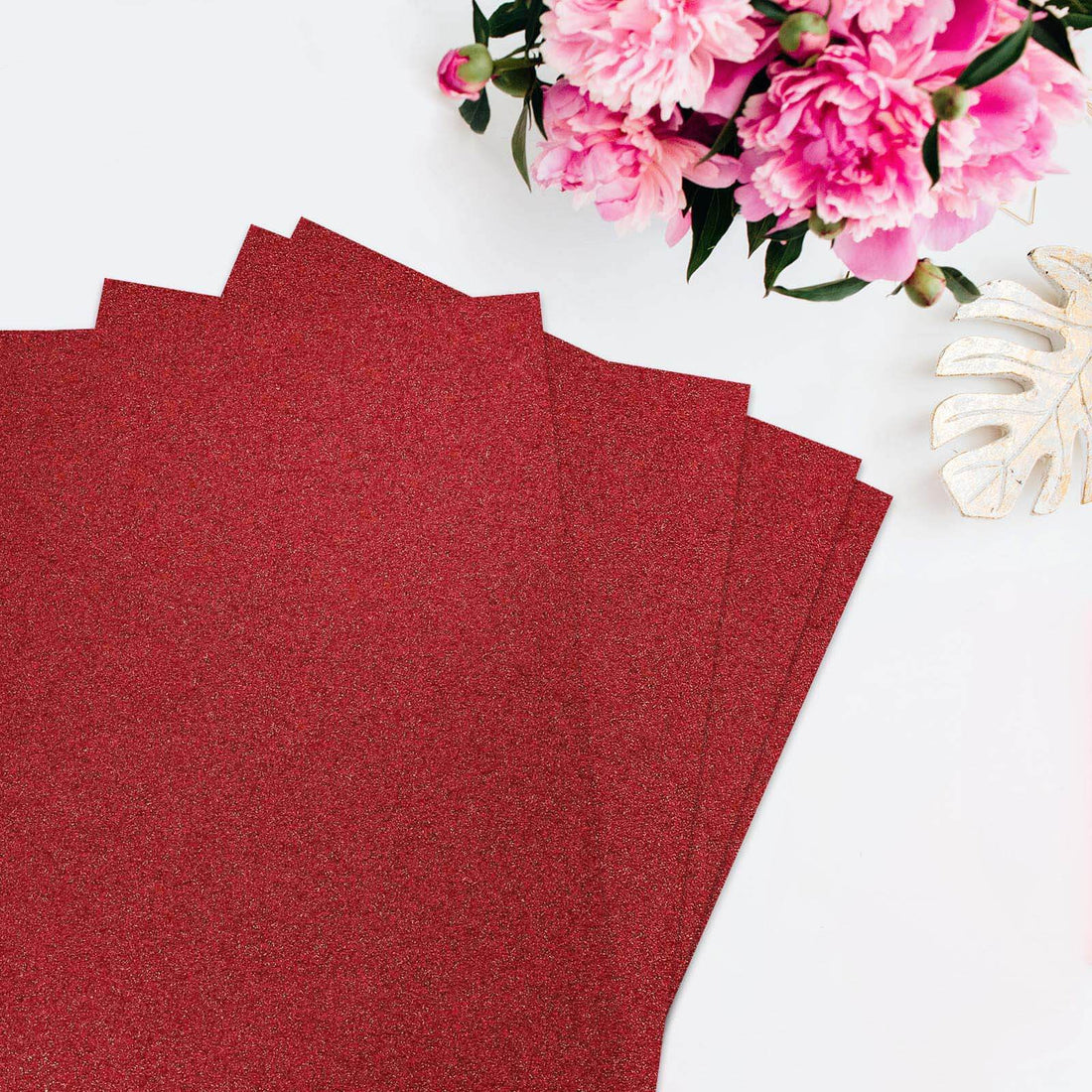 Red glitter cardstock sheets with pink flowers in the background.
