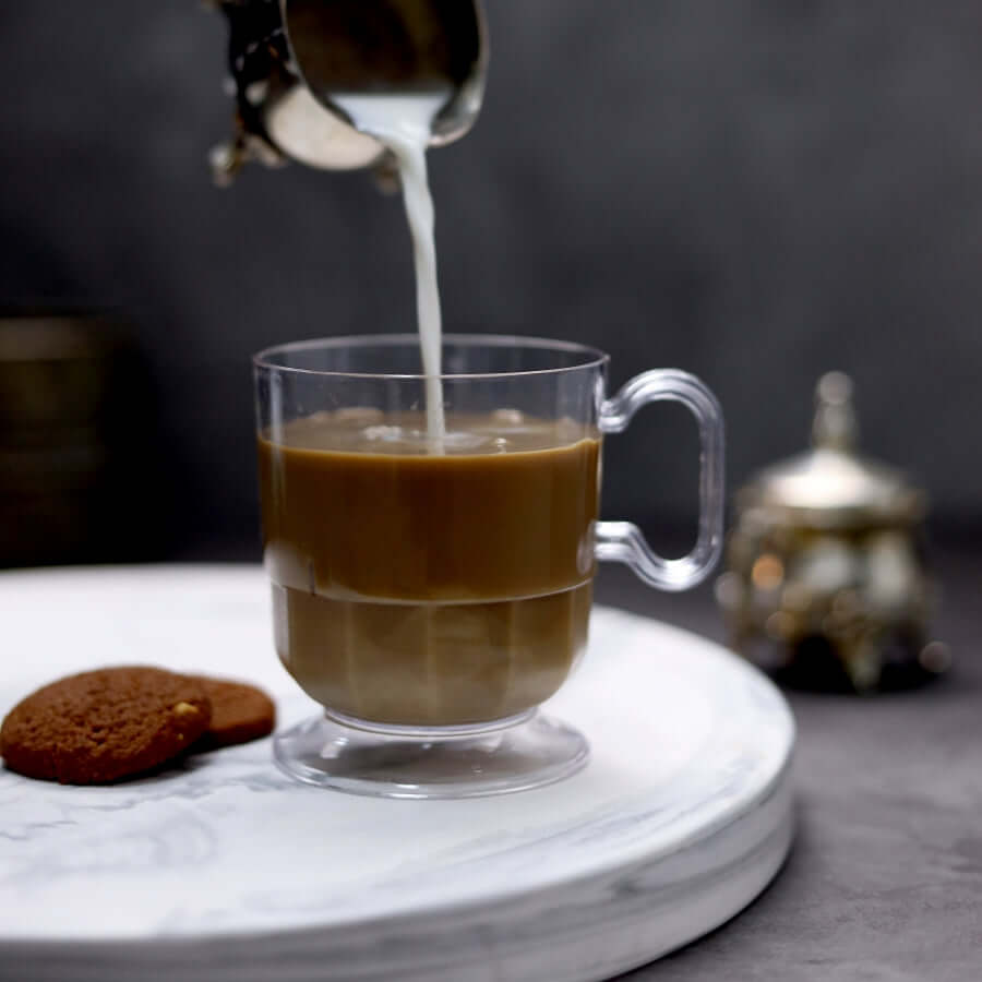 Clear coffee cup with milk being poured, accompanied by a cookie.