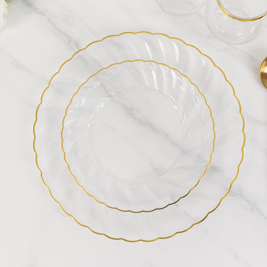 Clear plates with gold scalloped edges stacked on a marble surface.