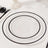 Clear glass plates with black rims in three sizes on a white table setting.