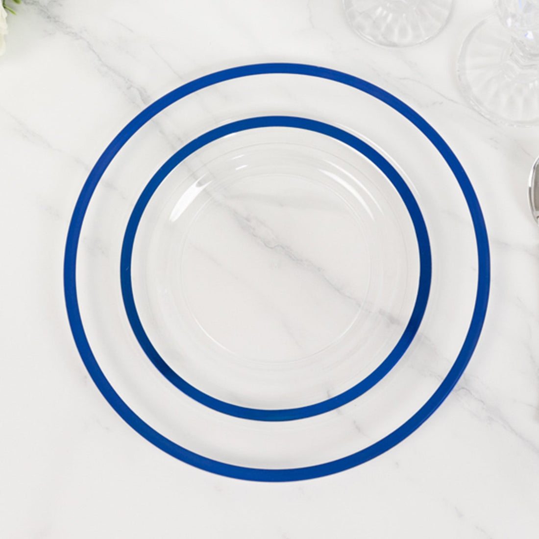 Clear plates with blue rims stacked on a marble surface.