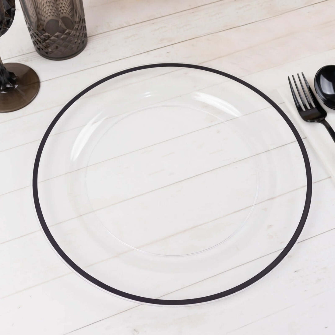 Clear plate with a black rim on a white wooden table.