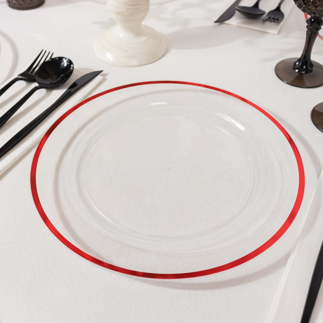 Clear plate with red rim on a stylish dining table setting.