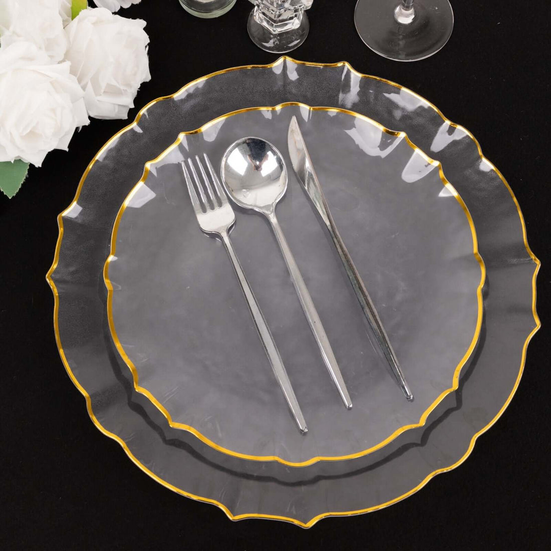 Elegant clear plate set with gold trim, fork, knife, and spoon on black background.