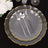 Elegant clear plate set with gold trim, fork, knife, and spoon on black background.