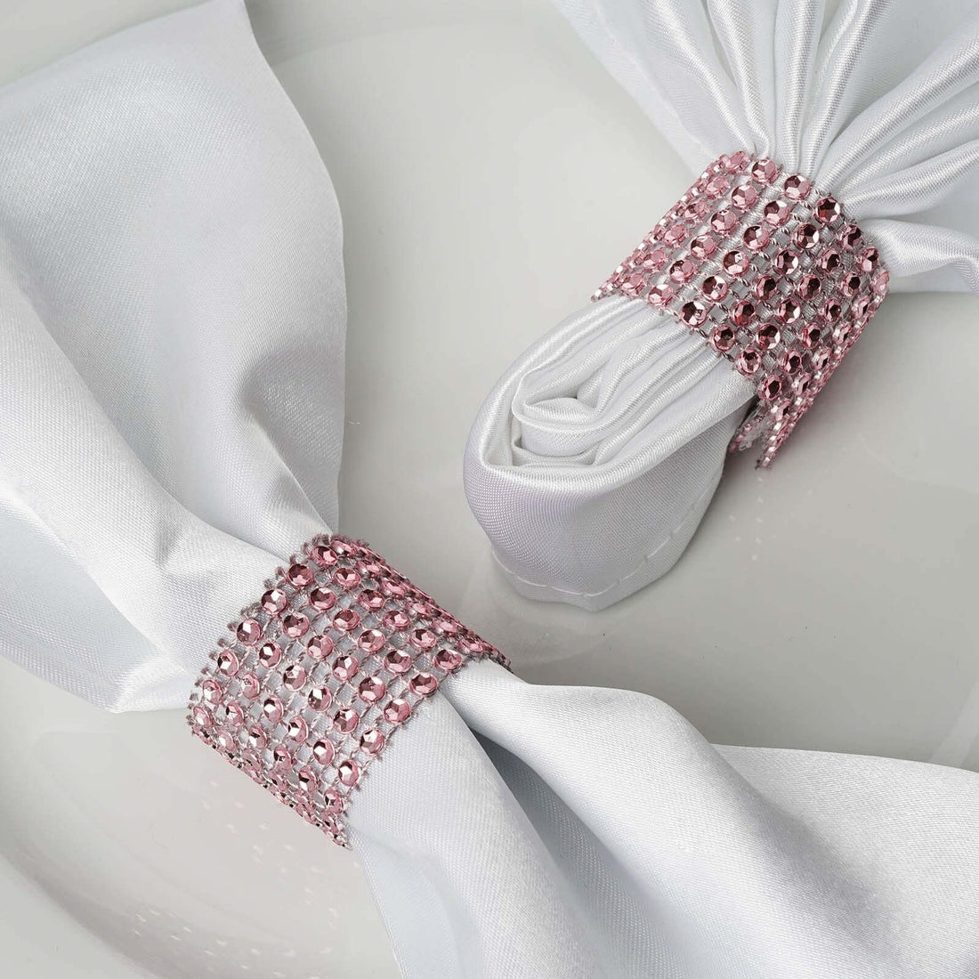 Elegant white napkins with pink jeweled holders on a plate.