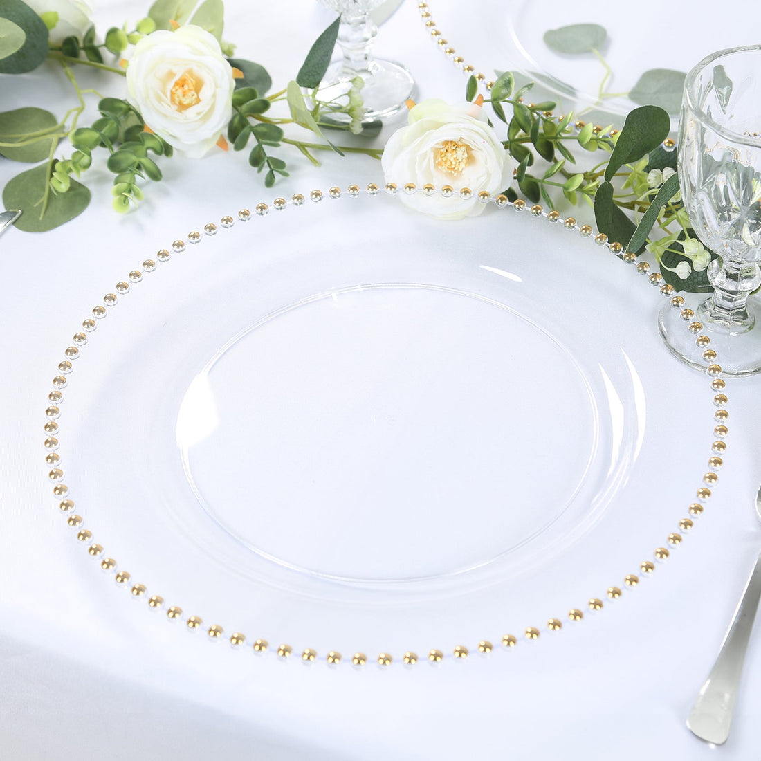 Clear glass charger plate with gold bead trim on white table setting.