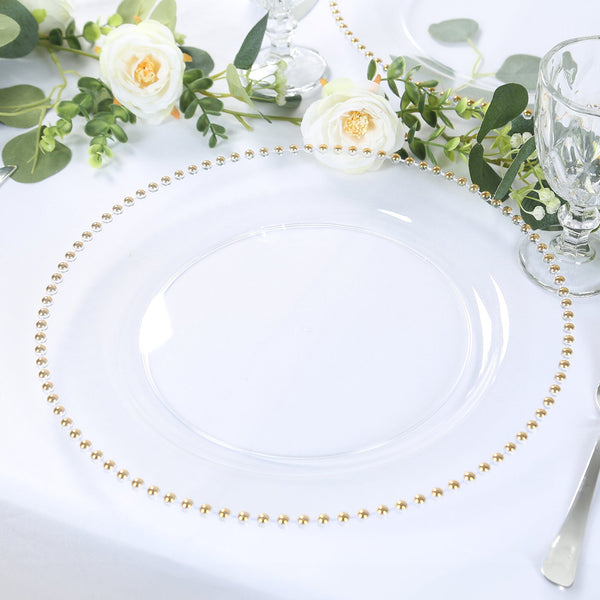 Clear glass charger plate with gold bead trim on white table setting.