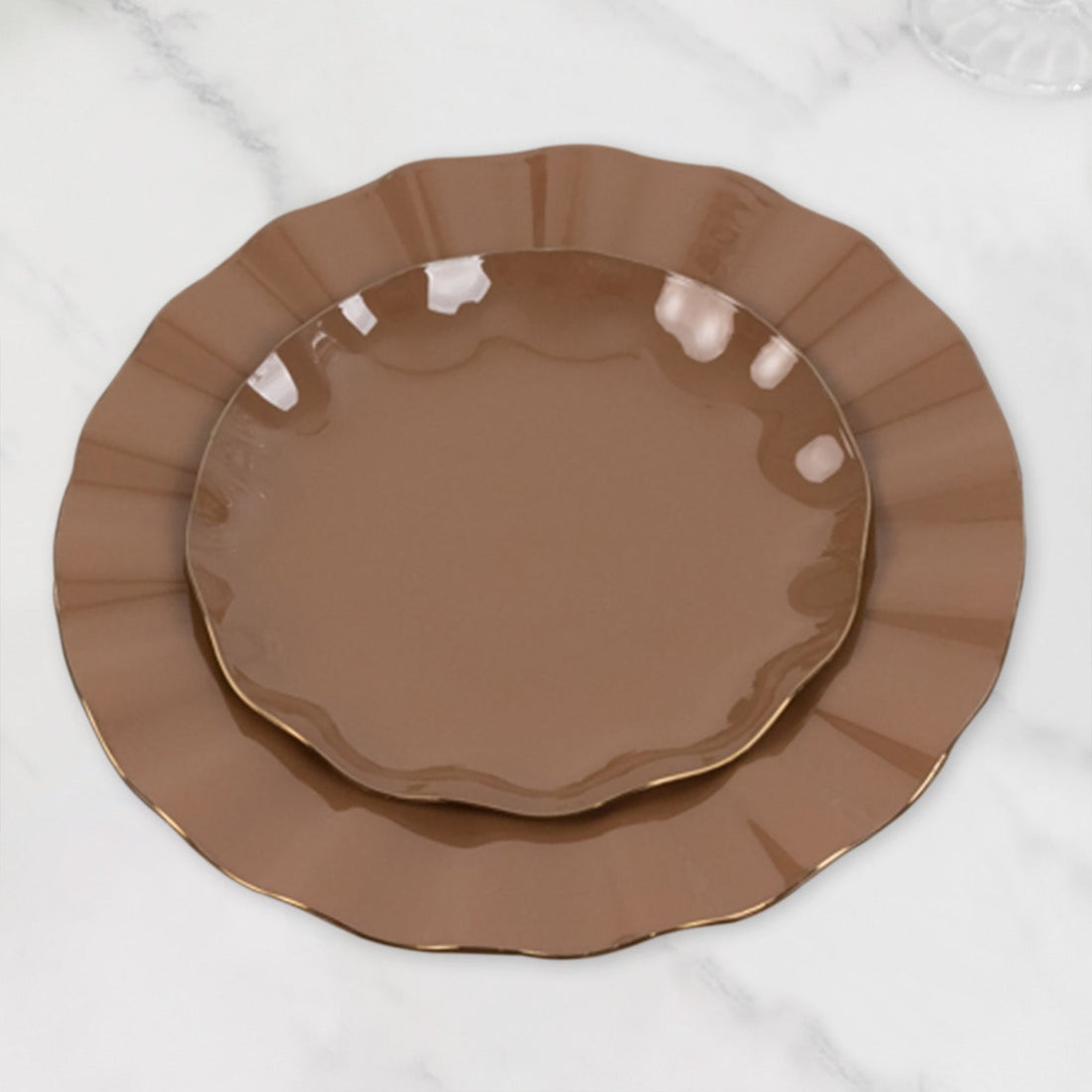 Brown ceramic plates with a scalloped edge and gold trim on a marble surface.