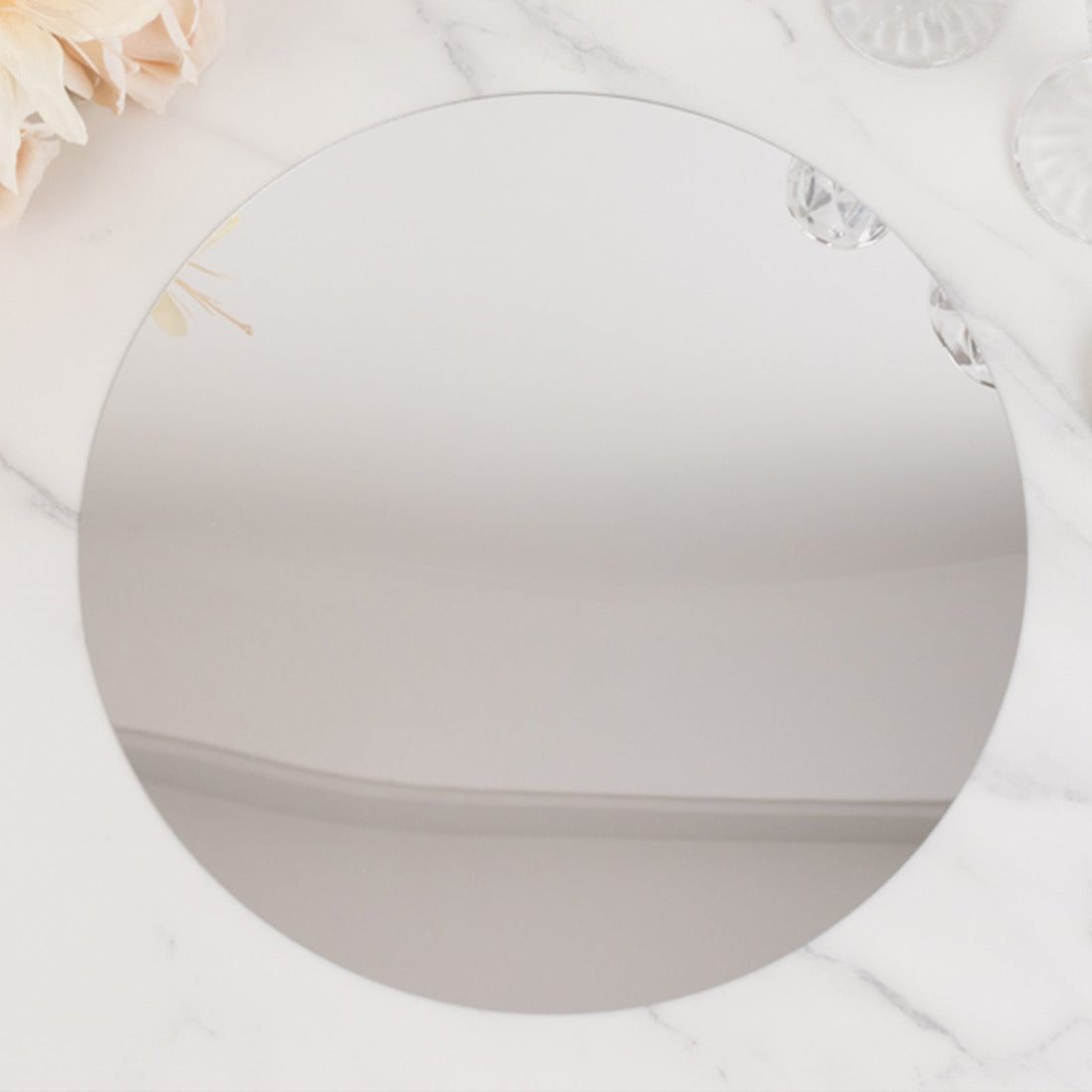 Round mirror on a marble surface, reflecting soft light and floral accents.