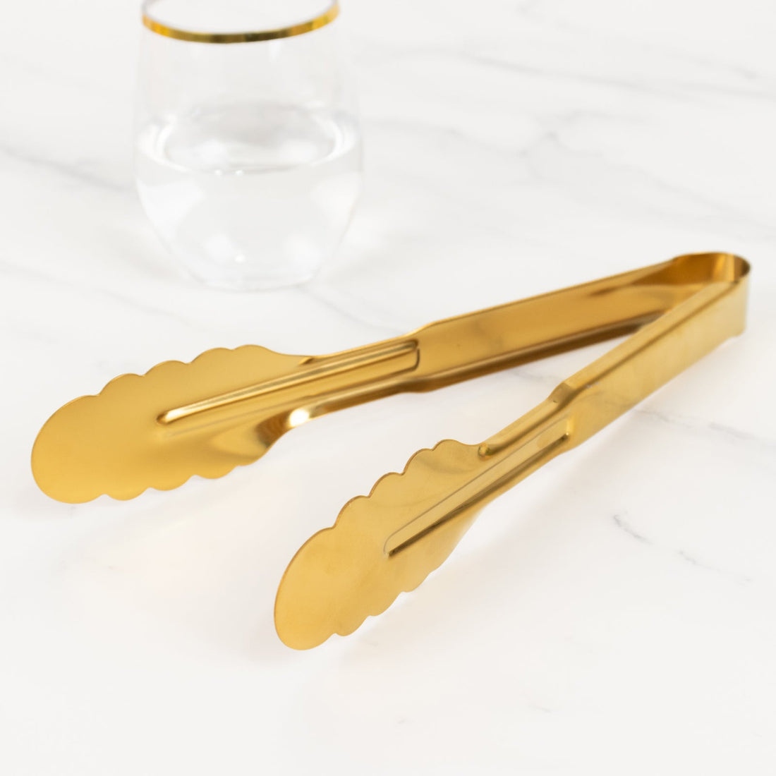 Gold serving tongs on a marble surface with a glass of water
