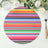 Colorful striped round placemat on a table setting with flowers and glass.