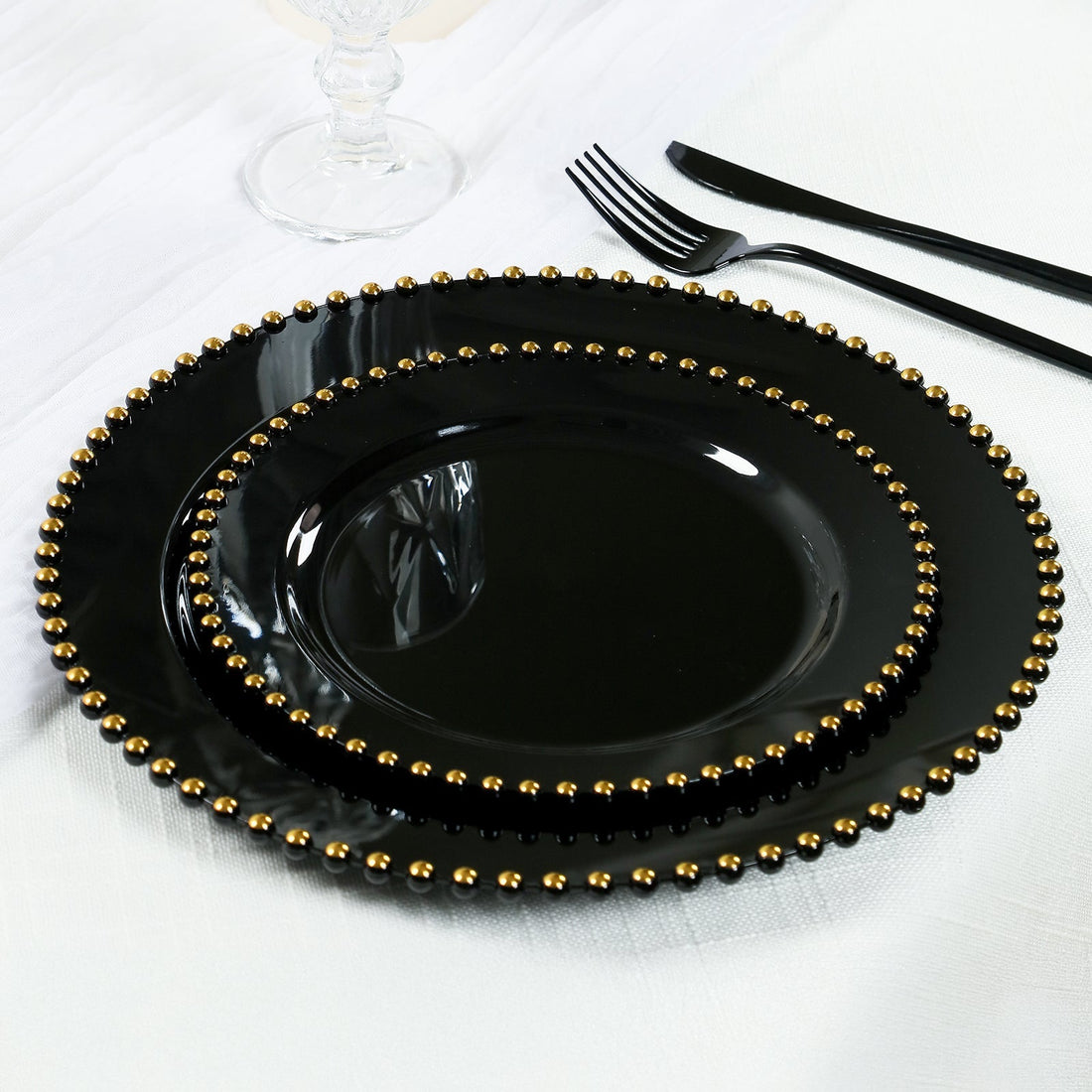 Black dinnerware set with gold beaded edges on a textured white tablecloth.