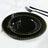 Black dinnerware set with gold beaded edges on a textured white tablecloth.