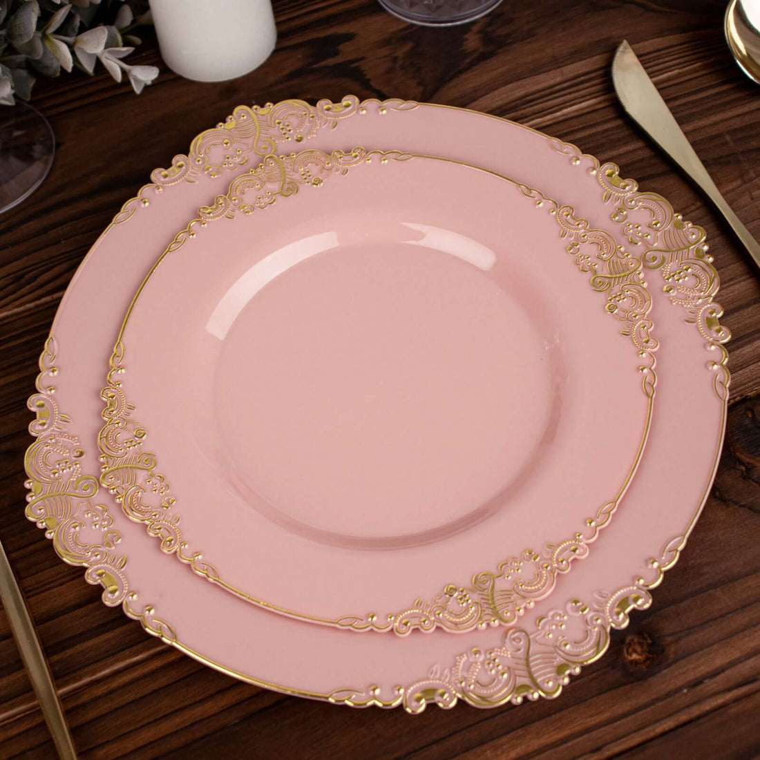 Elegant pink dinner plate with gold ornate details on rustic wooden table.