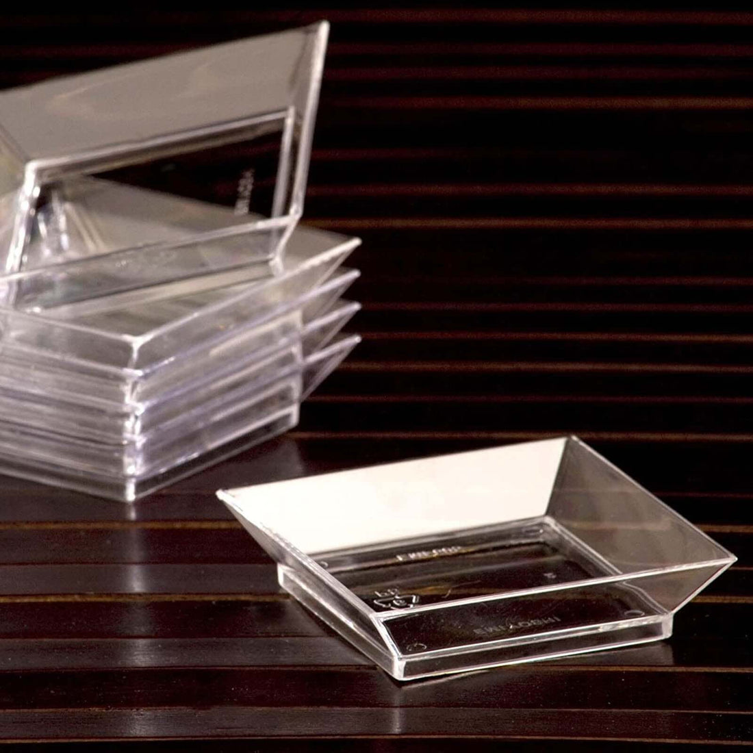 Clear acrylic serving dishes stacked on a wooden surface.