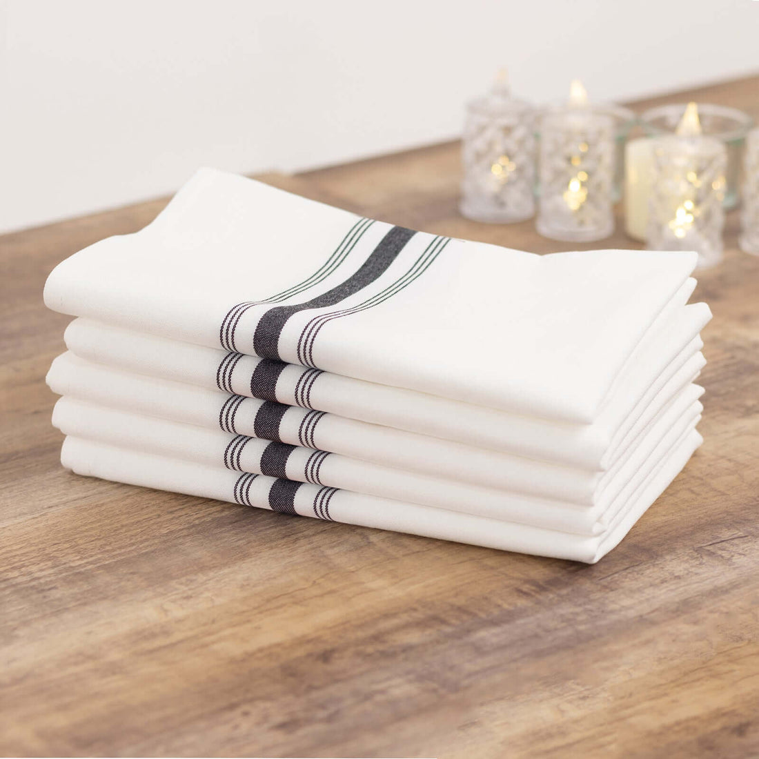 Stack of white kitchen towels with black and green stripes on a wooden table.