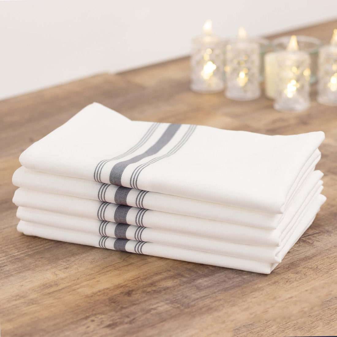 Stack of white kitchen towels with gray stripes on a wooden table.