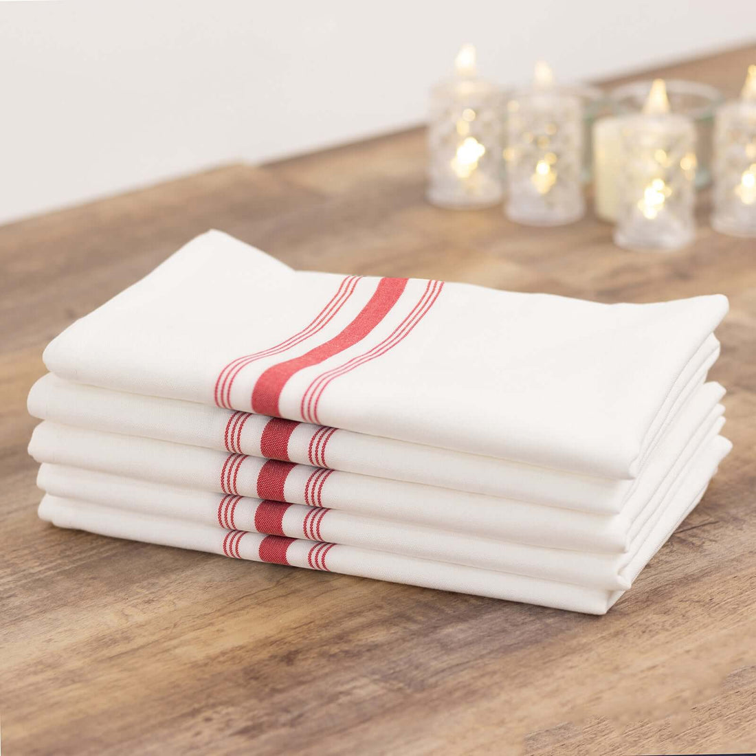 Stack of white kitchen towels with red stripes on a wooden table.
