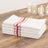 Stack of white kitchen towels with red stripes on a wooden table.
