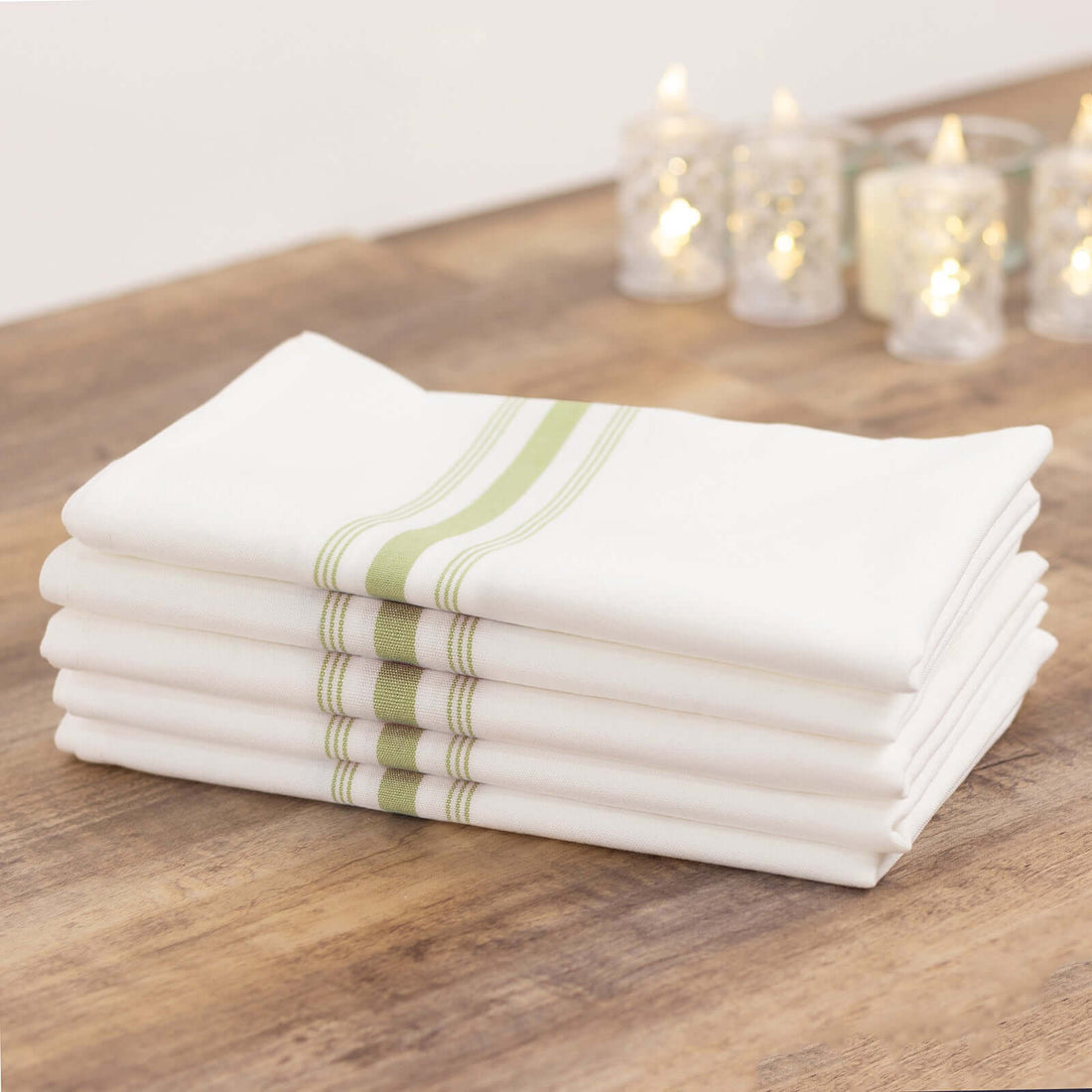 Stack of white kitchen towels with green stripes on a wooden table.
