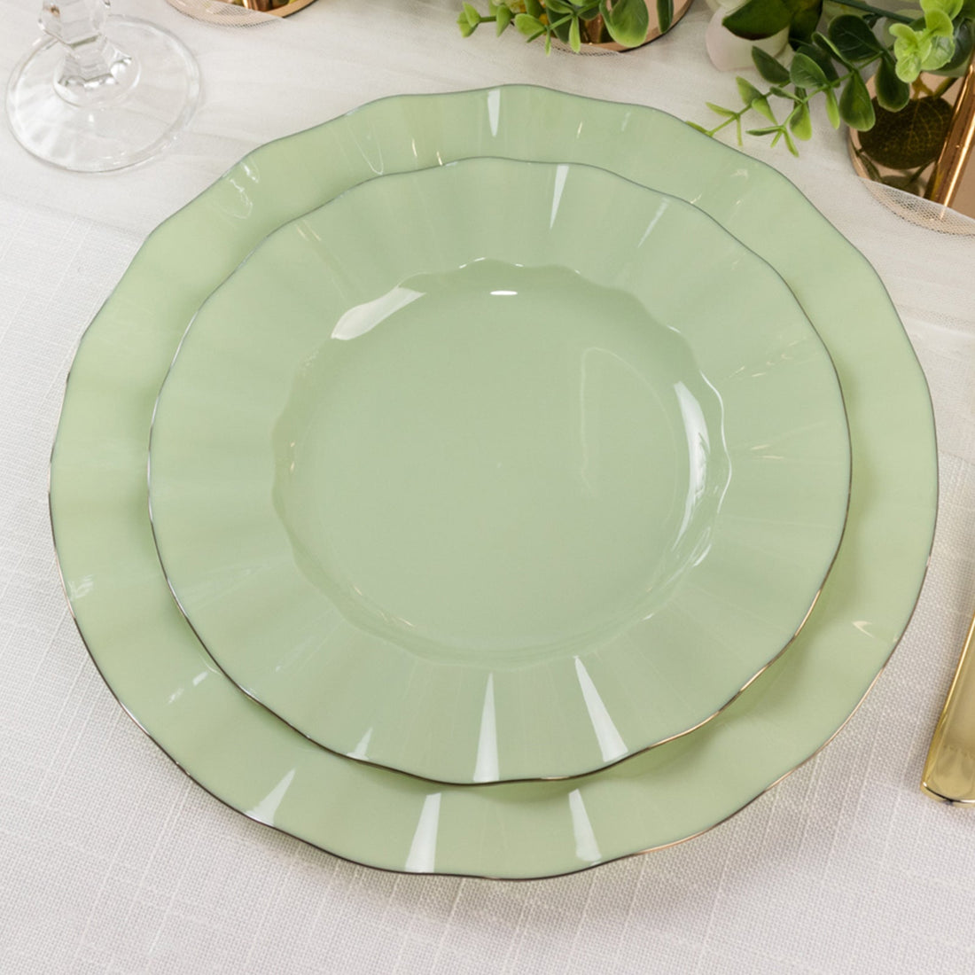 Green scalloped dinner plates stacked on a textured tablecloth.