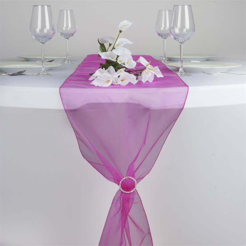 Purple table runner with floral decoration and wine glasses on a dining table. #whtbkgd