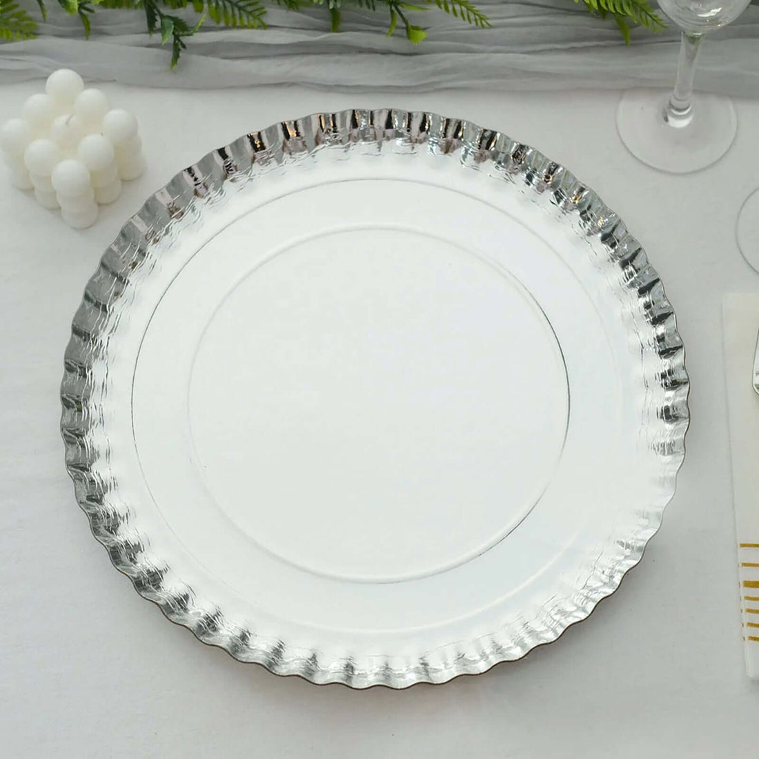 Silver decorative platter with scalloped edge on a white tablecloth.