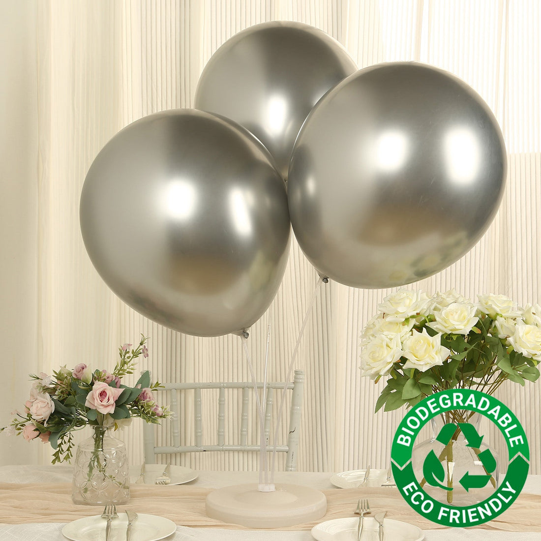Three silver biodegradable balloons on a table with flowers.