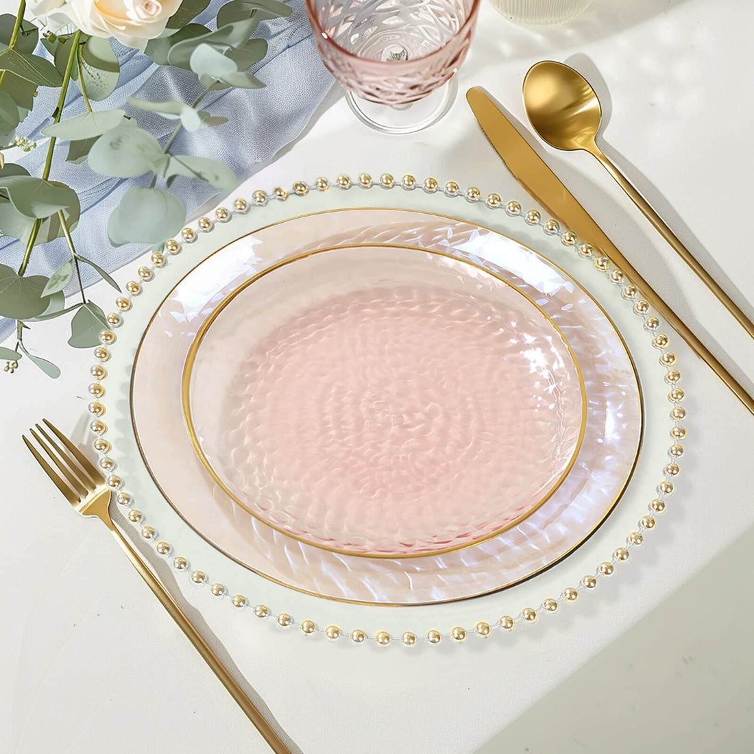 Elegant pink glass plate with gold trim on a beautifully set table.